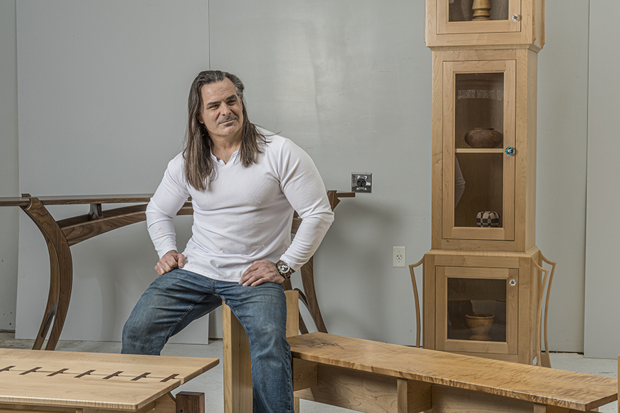 A man sits on a wooden bench in a room with tables and display cabinets made of wood.