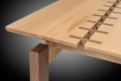 Close-up of a wooden table corner featuring interlocking joinery with contrasting wood tones against a dark gradient background.