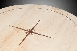 Round wooden tabletop with a compass rose design inlaid at the center and a thin dark border near the edge.