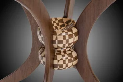 Close-up of an intricate wooden sculpture featuring curved arms and a checkered geometric sphere at the center.