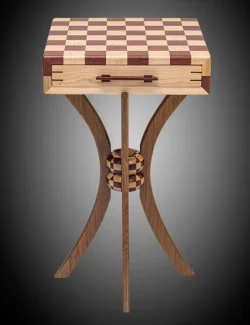 A wooden chess table with a checkered top, a central support column, and three curved legs against a dark background.