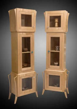 Two tall, light wood display cabinets with glass doors, each containing various pottery items on the shelves.