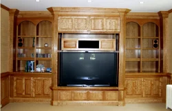 Built-in wooden entertainment center with shelves, cabinets, a large TV, and speakers on either side.