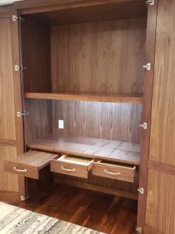 Empty wooden built-in cabinet with open doors and three open drawers, showing a shelf and a power outlet inside.