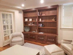 A wooden bookshelf with books, decor items, and cabinets stands against a wall in a modern living room.