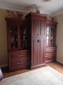 Large dark wood cabinet with glass doors and drawers, topped with animal figurines and art, stands against a beige wall.