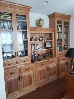 Wooden built-in bookshelf with glass doors, books, figurines, a lamp, decorative items, and a globe on top.