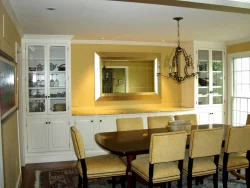 Dining room with a dark wood table, eight upholstered chairs, built-in cabinets, and a large wall mirror.