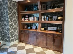 Built-in wooden bookshelf with books, photos, and decor items, set against a patterned wall and a checkered tile floor.