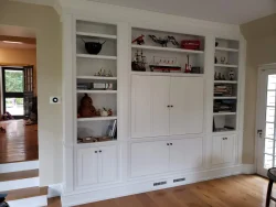 White built-in shelving unit with cabinets, books, ship models, and various decorative items in a living room.