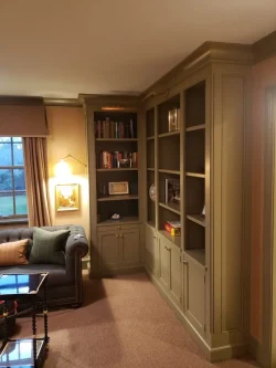 Built-in green bookshelves with cabinets and open shelves in a carpeted living room, next to a sofa and window.