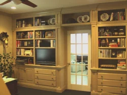 Built-in wooden shelves with books, drawers, a TV, and decorative plates surround a glass-paneled door in a home office.