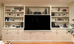 Built-in white shelves with holiday decorations and framed photos surround a large flat-screen TV in a living room.