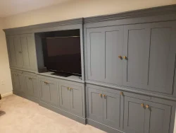 Gray built-in cabinets with gold handles, featuring a central open section holding a flat-screen TV and a small device.