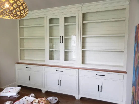 Large white built-in cabinet with glass doors, open shelves, and lower drawers, set against a light-colored wall.