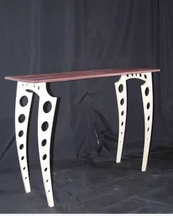 A narrow wooden table with curved, white legs featuring large circular cutouts, set against a black background.