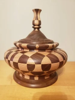 A wooden lidded container with geometric patterns in dark and light wood sits on a light-colored surface.