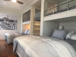 Room with two twin beds below and two bunk beds above, gray bedding, wooden floor, and a boat photo on the wall.