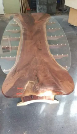 A wood and glass table with a live edge wooden center and clear glass extensions on both sides.