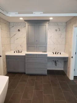 Modern bathroom with a double-sink vanity, gray cabinets, white countertops, and marble tile walls.