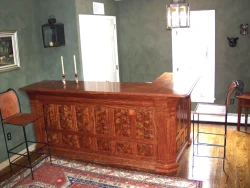 A wooden home bar with two chairs, two candlesticks, and a rug on a wooden floor in a room with green walls.