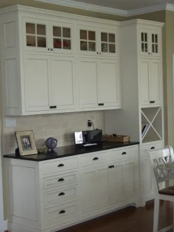 White kitchen cabinets with glass-front upper doors, black countertop, and beige tile backsplash in a home interior.