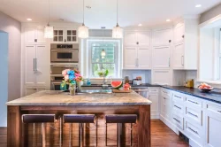 Modern kitchen with white cabinets, marble island, three barstools, and a vase of flowers on the countertop.