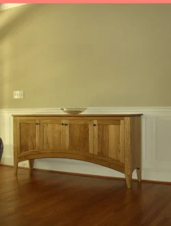 Wooden sideboard with four cabinet doors stands against a beige wall with white wainscoting and hardwood flooring.