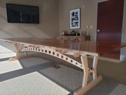Large wooden conference table with unique support beams in a modern office room with a TV and wall art.