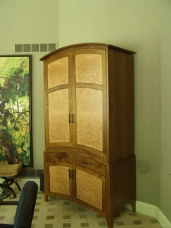 Tall wooden corner cabinet with two sets of double doors and two drawers, placed against a light-colored wall.