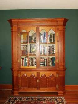 A wooden cabinet with glass doors displays books on shelves against a green wall and a patterned rug on the floor.