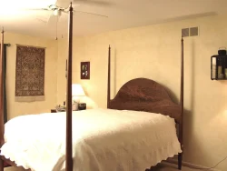 A bedroom with a four-poster bed, white bedspread, lamp on nightstand, and light yellow walls.