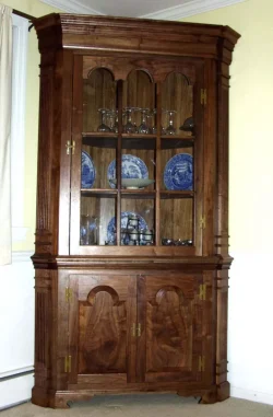 Wooden corner cabinet with glass doors displaying glassware and blue-patterned plates, with closed storage below.